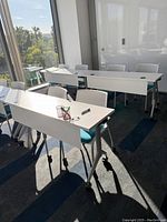 Photo of training room tables positioned near windows with scenic outdoor view, showing white tops, attached expansion leaves, and blue chairs.