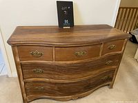 Front view of vintage curved front wooden dresser with brass handles and wear marks