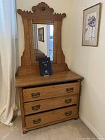 Full view of oak dresser with three drawers, ornate metal handles, and large mirror with carved wooden frame showing top decorative scroll work.