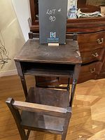 Front view of antique telephone table with chair placed underneath, showing worn dark wood surface and turned legs.