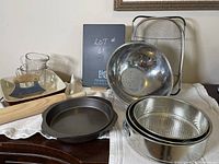 Photo showing the lot of baking and kitchen items neatly arranged including pans, colander, strainers, cutting board, and glassware