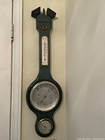 Full frontal view of the green wooden barometer with three integrated instruments hung on a white wall.