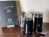 Three coffee-related items grouped together: Bodum coffee press on the left, Braun coffee grinder in the middle, and Nespresso grinder on the right. Black stand with lot number in background.