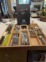 Wooden box containing various cutlery pieces including forks, knives, spoons, and ladles spread over multiple compartments.