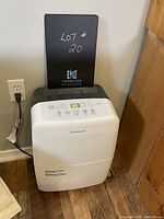 Full front and top view of white and gray Garrison portable dehumidifier plugged into wall outlet.