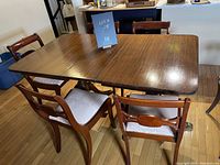 Wide shot of dated vintage wooden dining table with 6 chairs arranged around it.