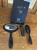Vanity set including hand mirror with ebony handle and frame, small rectangular brush, and large oval brush laid out on wooden surface