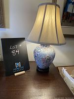 Floral table lamp on wooden base with lit fabric shade and lot sign beside it