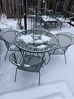 Green round metal patio table with matching chairs on a snowy outdoor surface.