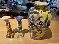 Front view of the vase and two candle holders on a countertop showing vibrant floral brushwork.