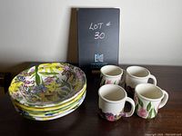 Photo showing four floral decorated bowls stacked and four mugs with floral tulip designs arranged on a wooden surface.