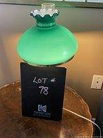 Green hurricane style lamp with ruffled white glass top and brass base, lit and unlit views