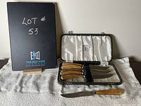 Opened case showing six steak knives with wood handles and stainless steel blades arranged inside satin-lined case and one knife outside