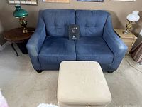 Side angle view of blue upholstered loveseat with white storage ottoman in front.