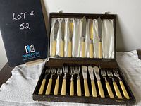 Closed original dark brown case with 12 piece flatware set, 6 knives and 6 forks with ivory or cream-colored handles, satin lining inside lid and base.