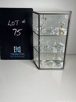 Overall front view of the glass and metal small curio cabinet with crystal animal figurines inside.