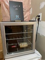 Mini silver Danby wine fridge with glass door showing two wire racks inside, containing two wine bottles horizontally.