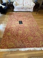 Top-down view of the rectangular pink wool rug with yellow floral pattern and fringe along the edge, placed on hardwood floor in living room.