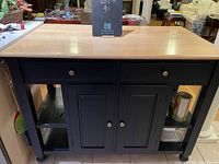 Front view of portable kitchen island showing pine top, two drawers, double doors, and shelves on both sides.