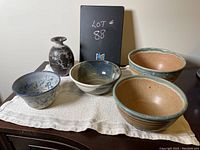Front view photo of all five pottery pieces including two large bowls, two smaller bowls, and a bud vase arranged on a cream textured cloth.
