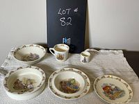 Five ceramic dinnerware pieces arranged on white cloth showing bunny illustrations and bunny borders