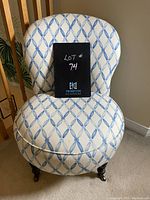 Front view showing curved back and seat upholstered in white and blue fabric, turned wood legs with casters