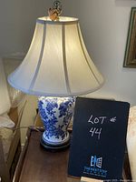 Front view of lamp lit on a wooden table with black lot sign next to it.