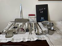 Full view of assorted stainless steel kitchen utensils laid out on white towel