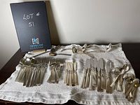 Full overview of the flatware laid on a white textured towel showing the bulk of the pieces arranged and visible.