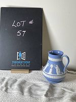 Full view of the Wedgwood blue jasperware jug with classical white reliefs, alongside a black sign indicating lot number 57.