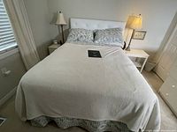 Full view of bed with upholstered white headboard and two boudoir lamps on each side on nightstands