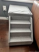Front view of collapsible pet stairs with cushioned ottoman top and three steps covered in light grey fabric.