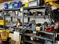 Two black metal shelving units side by side loaded with miscellaneous hardware