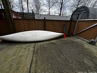 White silver canoe hull upside-down on concrete surface by fence