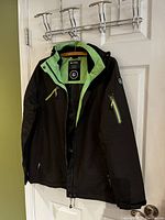 Black and light green Killtec ski jacket hanging on door hook, view of front showing zipper and pockets