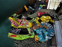 Four inflatable water tubes laid on the ground in an outdoor area, showing bright colors, multiple handles, and brand logos. Various sizes and designs visible.