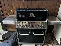 Front view of Broil King Baron gas BBQ grill showing black lid with logo, control knobs, and side burner