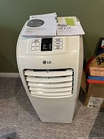 Front view of the LG portable air conditioner with control panel and included manuals on top.