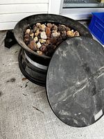 Side angle showing fire bowl with lava rocks inside and round metal cover leaning against it.