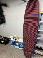 Surfboard upright inside red and navy striped fabric cover leaning against wall
