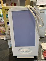 Front view of Verilux HappyLight lamp with power cord wrapped around it, showing blue light filter panel and control switches.