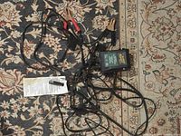 Full view of Battery Tender Junior charger showing attached wiring and clamps on patterned carpet.