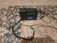 Full view of the black plastic Campbell Hausfeld 12 Volt inflator with air hose and power cord on patterned rug.