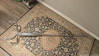 Full length photo of chrome coat hanger lying on patterned rug.