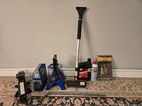 Full view of the vehicle emergency and maintenance kit including the jack, axle stand, tire compressor, engine oil, motor treatment, extendable brush, and tire repair kit in packaging