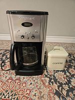 Photo of Cuisinart coffee maker and vintage coffee tin on patterned rug.