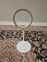 White desk lamp with circular metallic gold LED ring turned off, showing the ring shape and base charging pad.