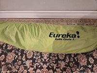 Green tent bag laid flat on patterned rug with “Eureka! Bella Coola 3” branding