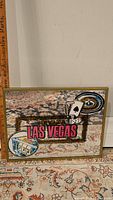 Framed mirror featuring Las Vegas and Nevada text with gambling symbols etched and printed on the glass, placed on a patterned carpet.