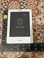 Kobo eReader powered off, showing 6 inch screen with white bezel and Kobo logo on top. Device placed next to ruler showing approximate dimensions.